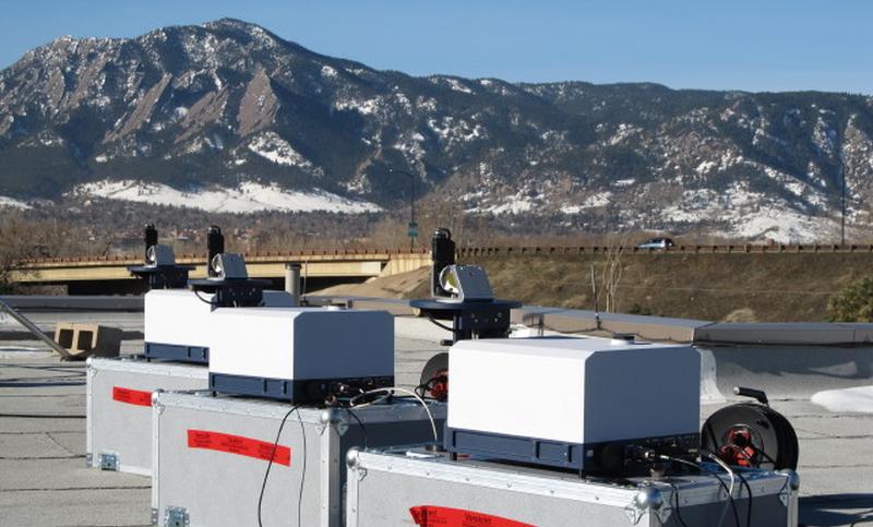 Drei wissenschaftliche Messgeräte auf einem Dach mit Bergpanorama und schneebedeckten Gipfeln.